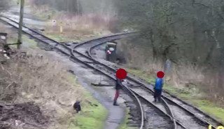 Two people having a conversation while trespassing on the railway with one stood foolishly in-between the rails, the other person is in an equally dangerous position.